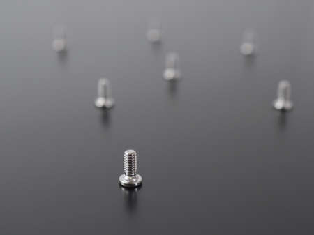 White screws stand on a dark matte surface. Background or wallpaper of small light bolts close-up. reduced contrast. Repair of electronic equipment and computer hardware. Macroの写真素材