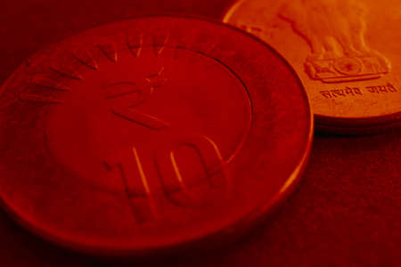 Translation: Truth Alone Triumphs. Two Indian coins lie on textured surface. 10 rupee coin with the...