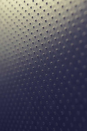 Tinted blue and yellow metal background. Dark vertical technical wallpaper. Perforated aluminum surface with many holes. Macroの写真素材