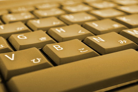 Japanese typing. Light brown laptop keyboard. Symbols on buttons of hiragana. Electronic commerce in Japan. IT technologies and data storage. Dark yellow tinted computer background or wallpaper. Macroの写真素材