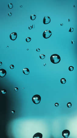 Raindrops on window glass. Abstract turquoise tinted background. natural mobile phone wallpaper. The...