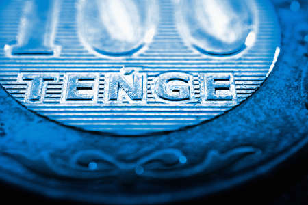 Translation: tenge. Fragment of Kazakh coin in 100 tenge. The name of the currency in Latin. Blue tinted illustration about economy of Kazakhstanの写真素材