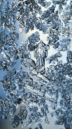 Ice crystals close up on a window glass in winter. Blue vertical background or phone wallpaper....