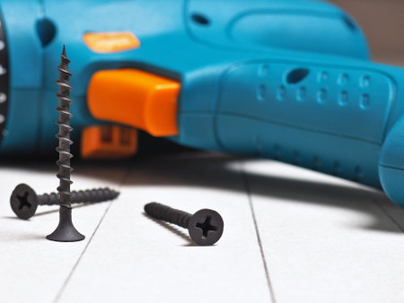 A screwdriver and screws lie on a sheet of gray drywall. Marking is applied to the sheet. Construction of houses, installation of walls and partitions, DIY repair. Focus on a standing screw. Macroの写真素材
