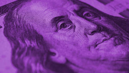 american paper money. A $100 bill with focus on eyes of Benjamin Franklin. Business economy and the USA dollar. US banknote close up. Franklin dollar note. Bright violet tinted background. Macroの写真素材