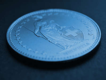 1 Swiss Franc coin closeup. Blue tinted background or backdrop about economy, business or banking. Money and Central Bank in Switzerland. Blurred figure of Helvetia, focus on the cross. Macroの写真素材