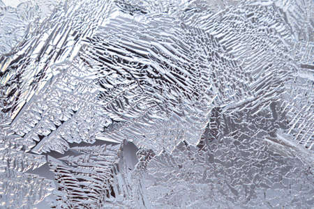 Ice and frost on a window pane in winter. Pattern from the leaves of fantasy plants. Crystals of...