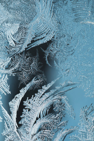 Abstract christmas background. Ice crystals on frozen window glass. Frost drawing. A pattern of leaves and stems of magical plant. Blue tinted winter wallpaper. cold and crystal. Macroの写真素材