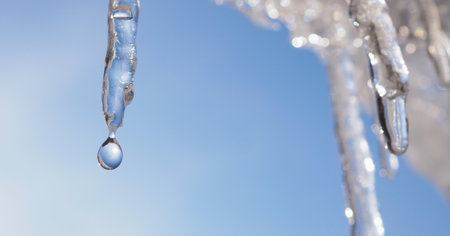 Icicle against light blue sky. Drop of melted snow falls down. close up. Horizontal stories about beginning of spring. Winter thaw. Macroの写真素材