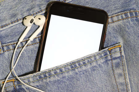 Template for music content. A smartphone with a white screen and earphones in the pocket of blue jeans.の写真素材