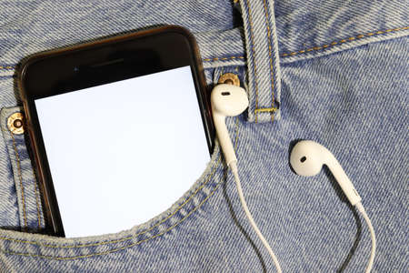 Template for audiovisual content. Place to insert illustration of a podcast or song. Smartphone with a white screen and earphones in the pocket of blue jeans.の写真素材