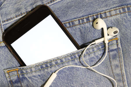 Template for audio and video content. Phone with a white screen and headphones in a jeans pocket....
