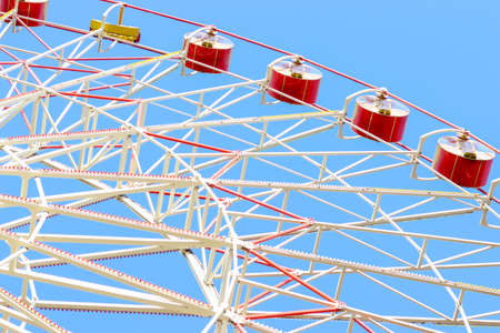 The big ferris wheel moves. Bright photo of the amusement park. Red cabins against a clear blue sky. Ferris wheel in the park. The concept of entertainment, joy, pleasure and celebration.の写真素材