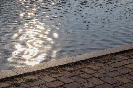 Water surface with reflection of light rays with asphalt nearby. The concept of tourism, tranquility and relaxation. Copy space for text.の写真素材