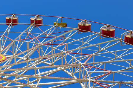 Big ferris wheel moves. Bright photo of the amusement park. Red cabins against a clear blue sky. Ferris wheel in the park. Concept of entertainment, joy, pleasure and celebration. Copy space for text.の写真素材