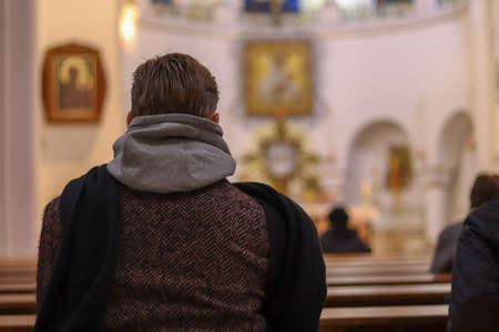 Man in coat from the back close up in Catholic church. Bokeh effect with blur background. Copy space for text. Concept on the theme of faith, religion and church. Men praying.の写真素材