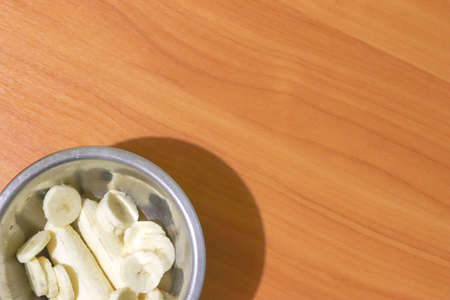 Banana slices in a metal plate on a wooden table with copy space. Top view of tropical fruits and healthy eating.の写真素材