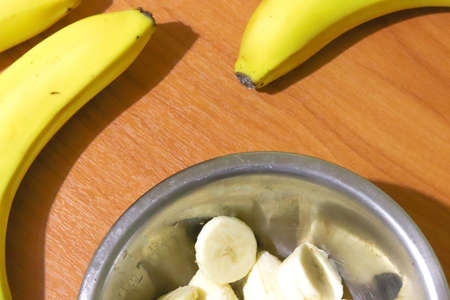 Top view of bananas on a wooden table with sliced bananas in a metal plate. Proper nutrition of healthy foods. Background for placing text.の写真素材