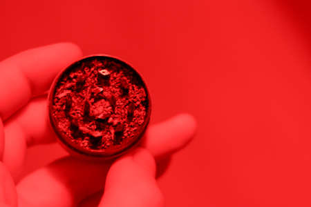Grinder with marijuana in hand close-up. Red lighting. Copy space and blurred background. Medical drug use.の写真素材