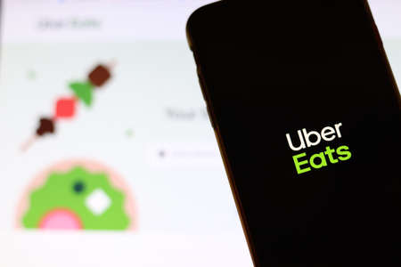 Los Angeles, California, USA - 21 November 2019: Uber Eats logo on phone screen with icon on laptop on blurry background, Illustrative Editorial.のeditorial素材