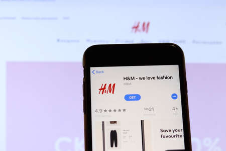 Los Angeles, California, USA - 27 November 2019: HM app icon on mobile phone screen with blurry website on laptop, Illustrative Editorial.のeditorial素材