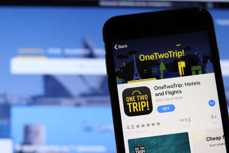 Los Angeles, California, USA - 27 November 2019: OneTwoTrip app icon on mobile phone screen with blurry website on laptop, Illustrative Editorial.のeditorial素材