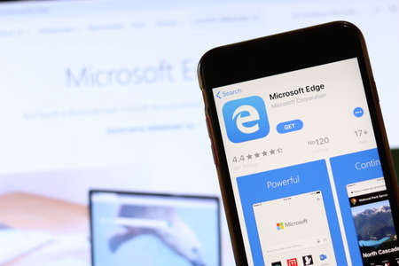 Phone with Microsoft Edge icon on screen close up with blur website on laptop. Los Angeles, California, USA - 30 November 2019, Illustrative Editorial.のeditorial素材