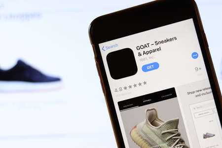 Phone with GOAT Sneakers app icon on screen close up with blur website on laptop. Los Angeles, California, USA - 30 November 2019, Illustrative Editorial.のeditorial素材