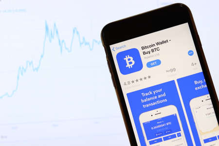 Phone with Bitcoin Wallet app icon on screen close up with blur website on laptop. Los Angeles, California, USA - 30 November 2019, Illustrative Editorial.のeditorial素材