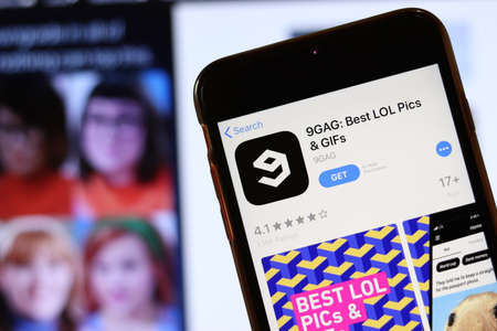 Phone with 9GAG icon on screen close up with blur website on laptop. Los Angeles, California, USA - 30 November 2019, Illustrative Editorial.のeditorial素材