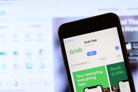 Phone with Grab App icon on screen close up with blur website on laptop. Los Angeles, California, USA - 30 November 2019, Illustrative Editorial.のeditorial素材