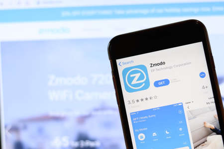 Phone with Zmodo icon on screen close up with blur website on laptop. Los Angeles, California, USA - 30 November 2019, Illustrative Editorial.のeditorial素材