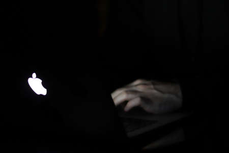 Saint-Petersburg, Russia - 10 December 2019: Man hands on apple laptop keyboard in dark room at...