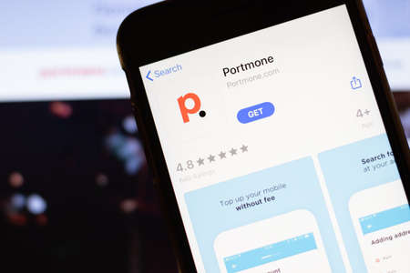 Los Angeles, California, USA - 12 February 2020: Mobile phone with Portmone icon on screen close up with website on laptop. Blurred background with Portmone.com site, Illustrative Editorial.のeditorial素材