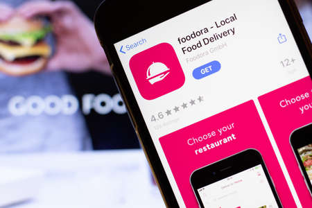 Los Angeles, California, USA - 12 February 2020: Mobile phone with Foodora icon on screen close up with website on laptop. Blurred background with foodora food delivery site, Illustrative Editorial.のeditorial素材