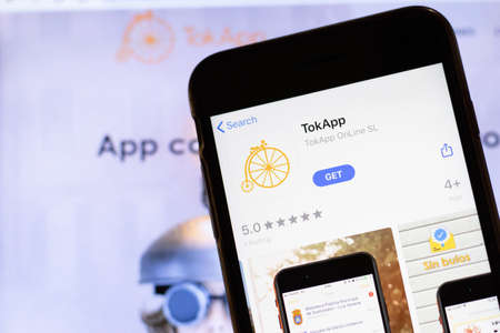 Los Angeles, California, USA - 12 February 2020: Mobile phone with TokApp icon on screen close up with website on laptop. Blurred background with TokApp.com site, Illustrative Editorial.のeditorial素材