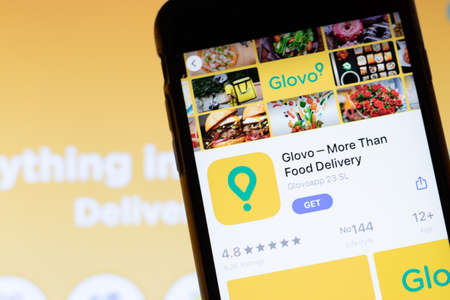 Los Angeles, California, USA - 12 February 2020: Mobile phone with Glovo icon on screen close up with website on laptop. Blurred background with Glovoapp site, Illustrative Editorial.のeditorial素材