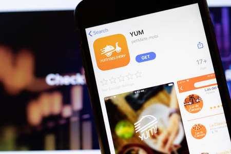Los Angeles, California, USA - 12 February 2020: Mobile phone with YUM icon on screen close up with website on laptop. Blurred background with Yum Delivery site, Illustrative Editorial.のeditorial素材