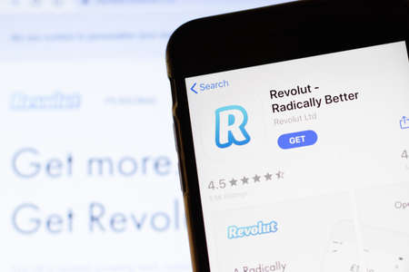 Los Angeles, California, USA - 12 February 2020: Mobile phone with Revolut icon on screen close up with website on laptop. Blurred background with Revolut.com site, Illustrative Editorial.のeditorial素材