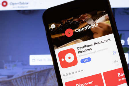 Los Angeles, California, USA - 12 February 2020: Mobile phone with OpenTable icon on screen close up with website on laptop. Blurred background with Opentable.com site, Illustrative Editorial.のeditorial素材