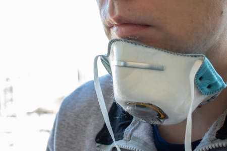 A man in a half-removed medical face mask. Respirator on the neck. Man head side view close-up with copy space.の写真素材