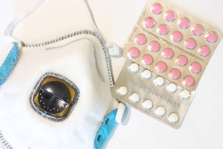Respirator on white background with tablets or pills top view. Medical mask flat lay.