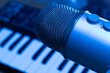 Music tracks production concept. Studio with microphone and synth keyboard on background in blue light.の写真素材
