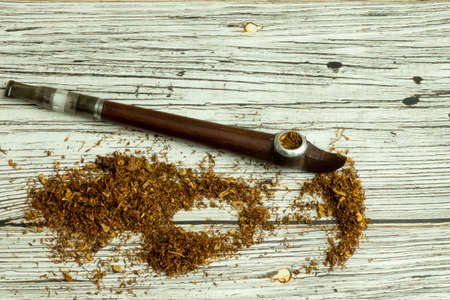Piled tobacco on the table with smoking pipe top view.