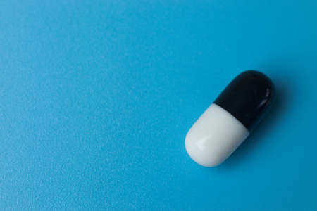 Black and white pill close up on blue background, copy space. Pharmaceutical industry.の写真素材