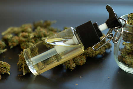 CBD extract in bottle. Hemp organic oil for medical use. Cannabidiol and THC. Marijuana buds on desk close-up.の写真素材