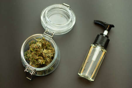 CBD herbal oil with cannabis buds in glass jar top view. Marijuana on black background. Weed business industry concept. Cannabidiol medical and recreational healthcare using.の写真素材