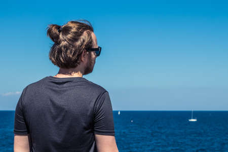 Guy with long hair looking at blue sea. Tourism concept, freelancer and copy space.