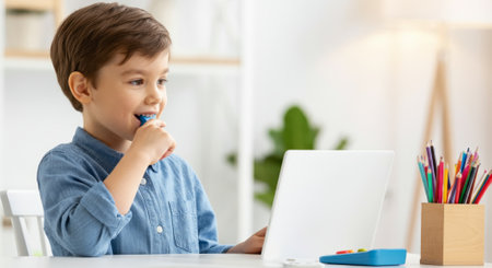 Boy is sitting at a table with a tablet and a box of crayons. He is brushing his teethの素材