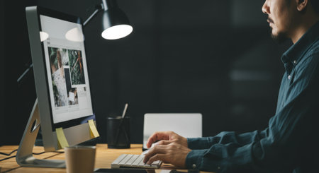 Man is typing on a computer. The computer monitor is on and the man is using a keyboardの素材